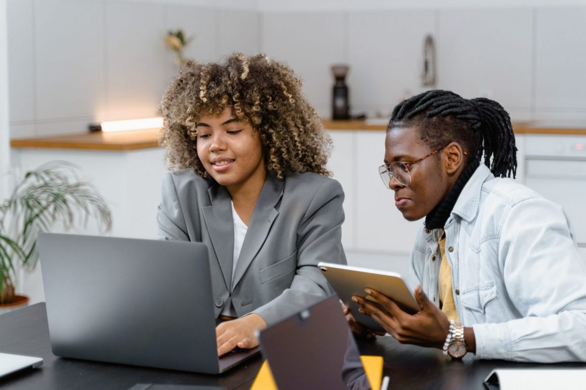 Two Black employees review performance or personality review, sitting in front of a computer in the office.