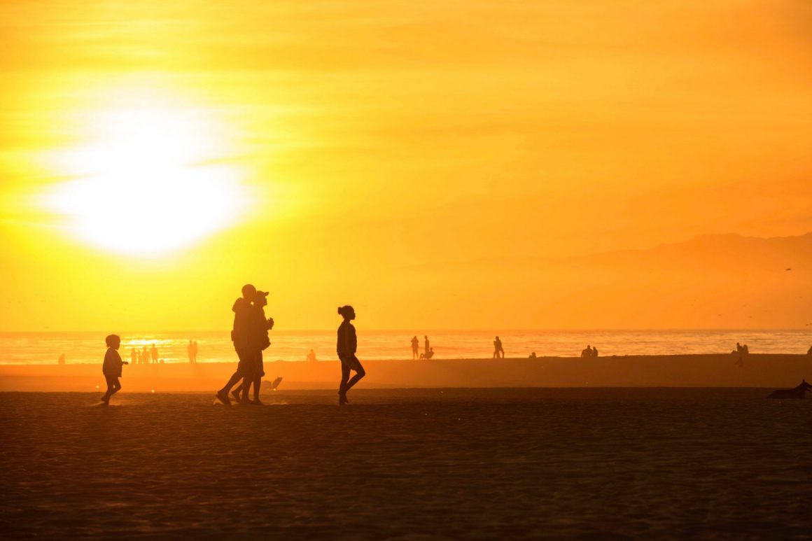 Black people walking on a Santa Monica beach as the sun sets.